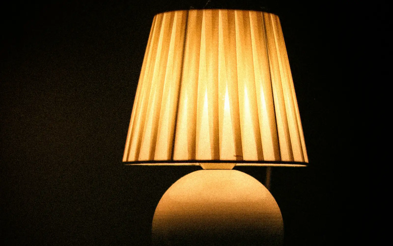 A pleated lamp glowing warm in a dark room