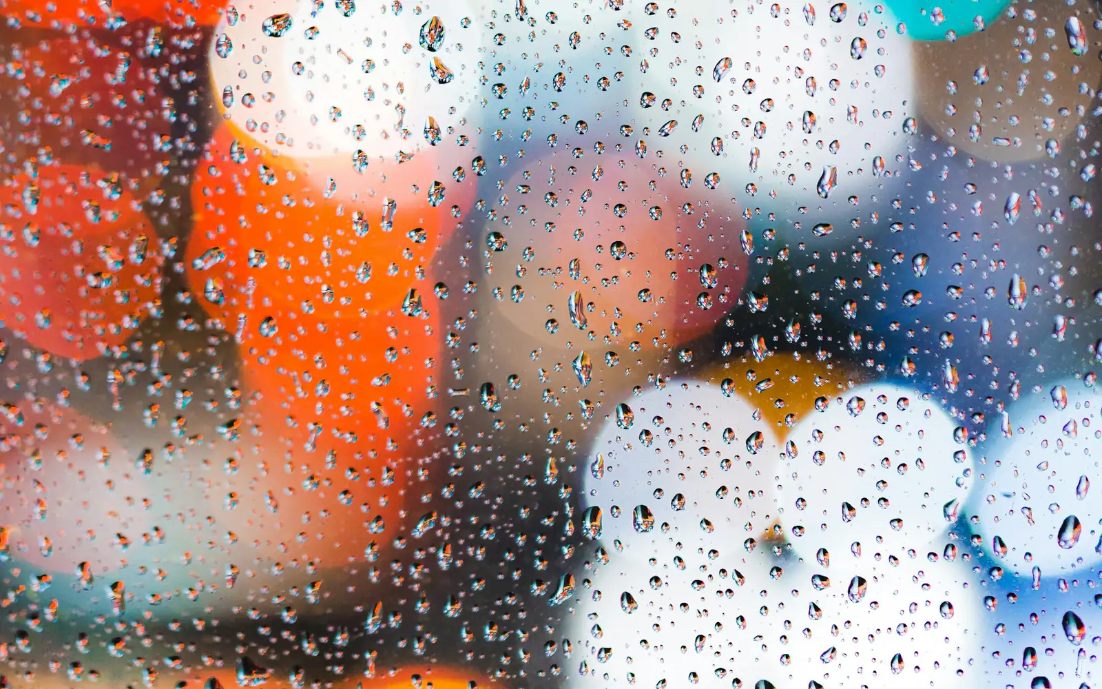 Raindrops on a window in front of blurred coloured lights