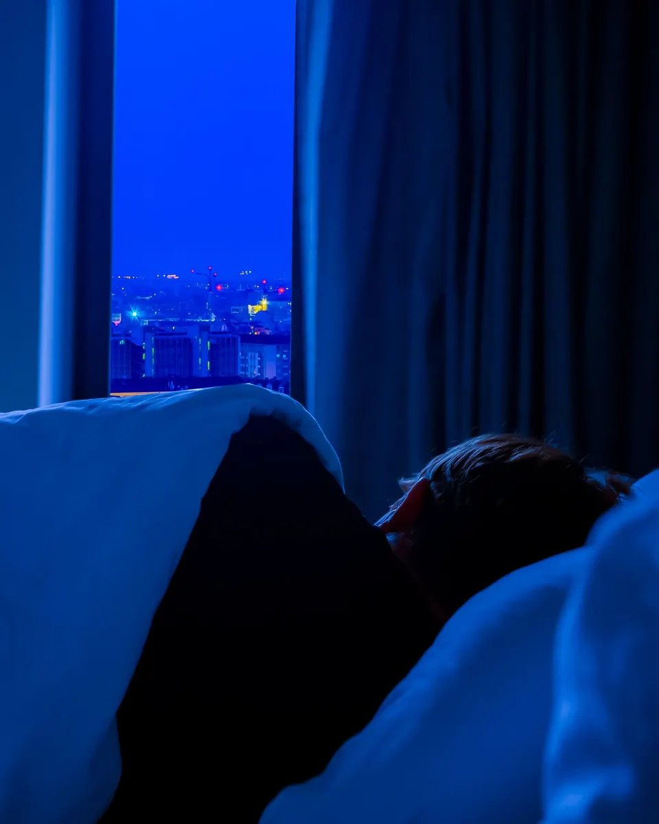 Someone asleep under a duvet, the city lit blue through the window